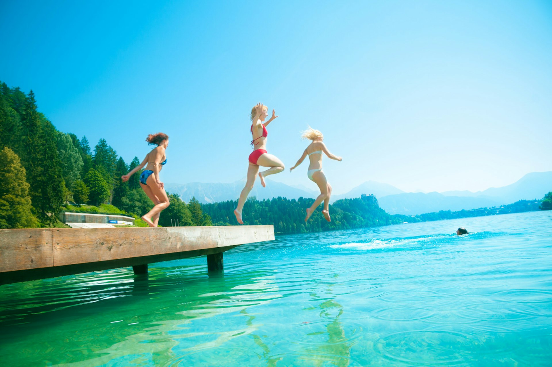 Three girls jump into Lake Bled, Slovenia on a summer's day