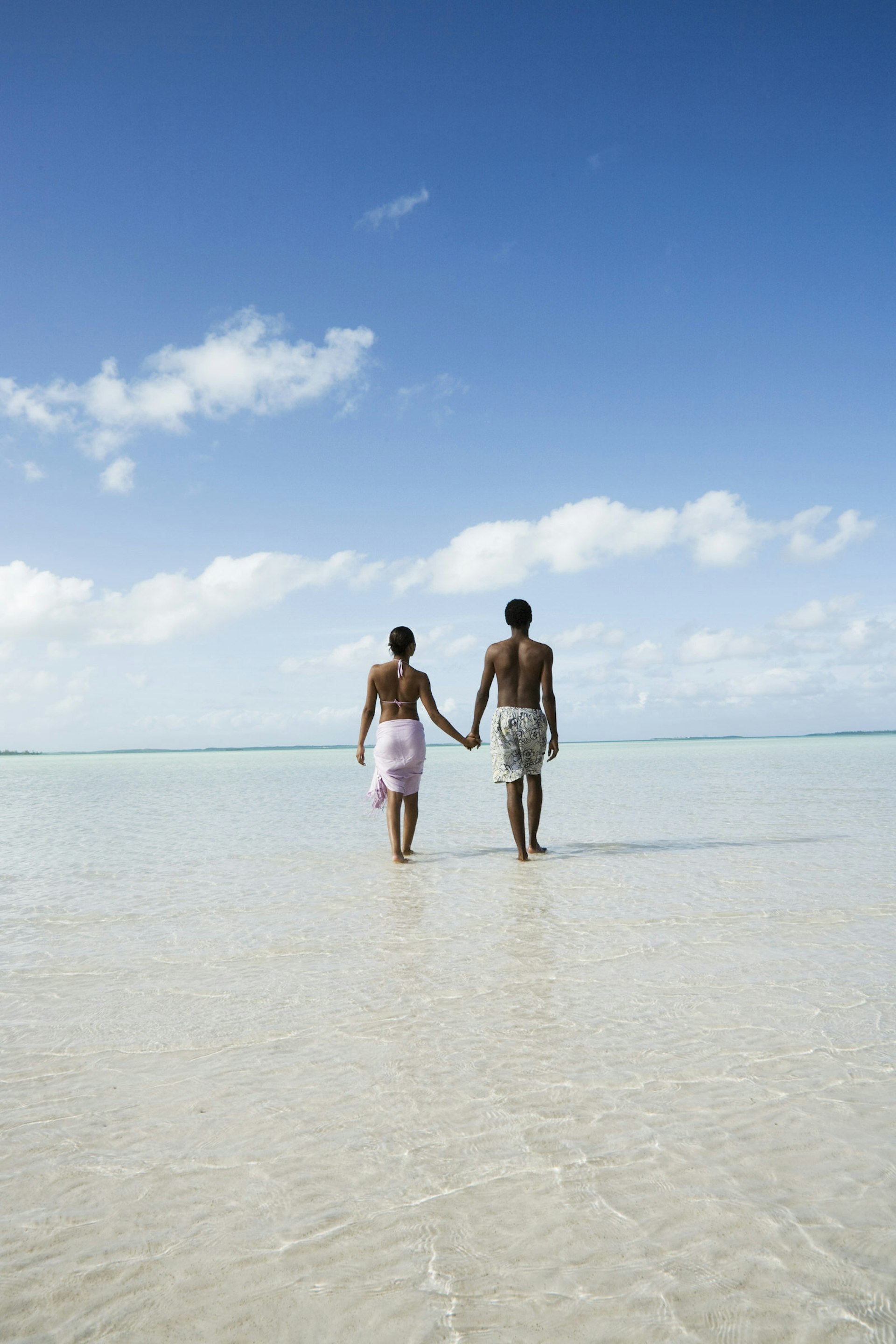 wedding anniversary trip ideas - A couple walk in the ocean shallows under a blue sky, Bahamas.