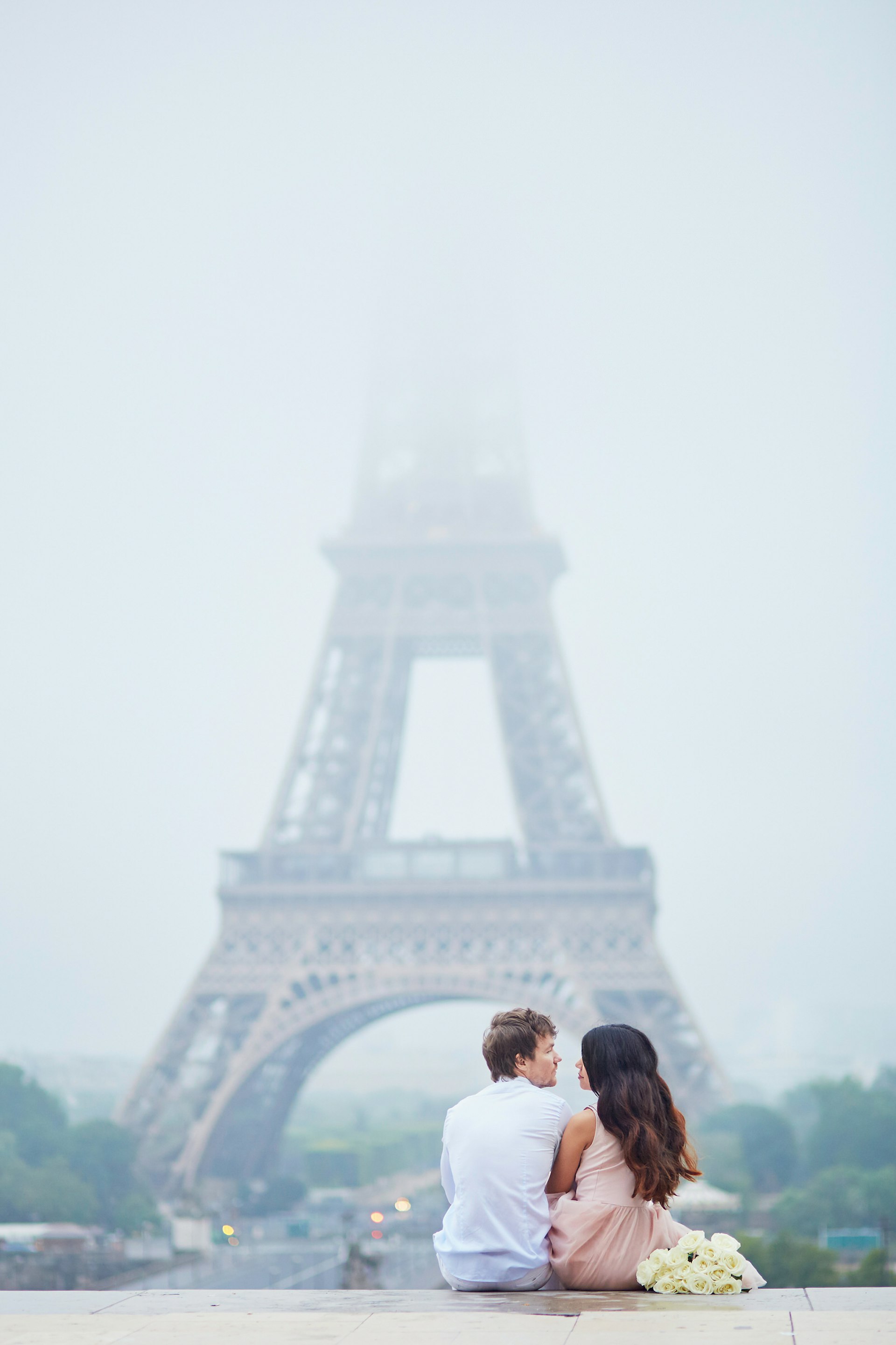 A couple post in front of the fog-shrouded Eiffel Tower.