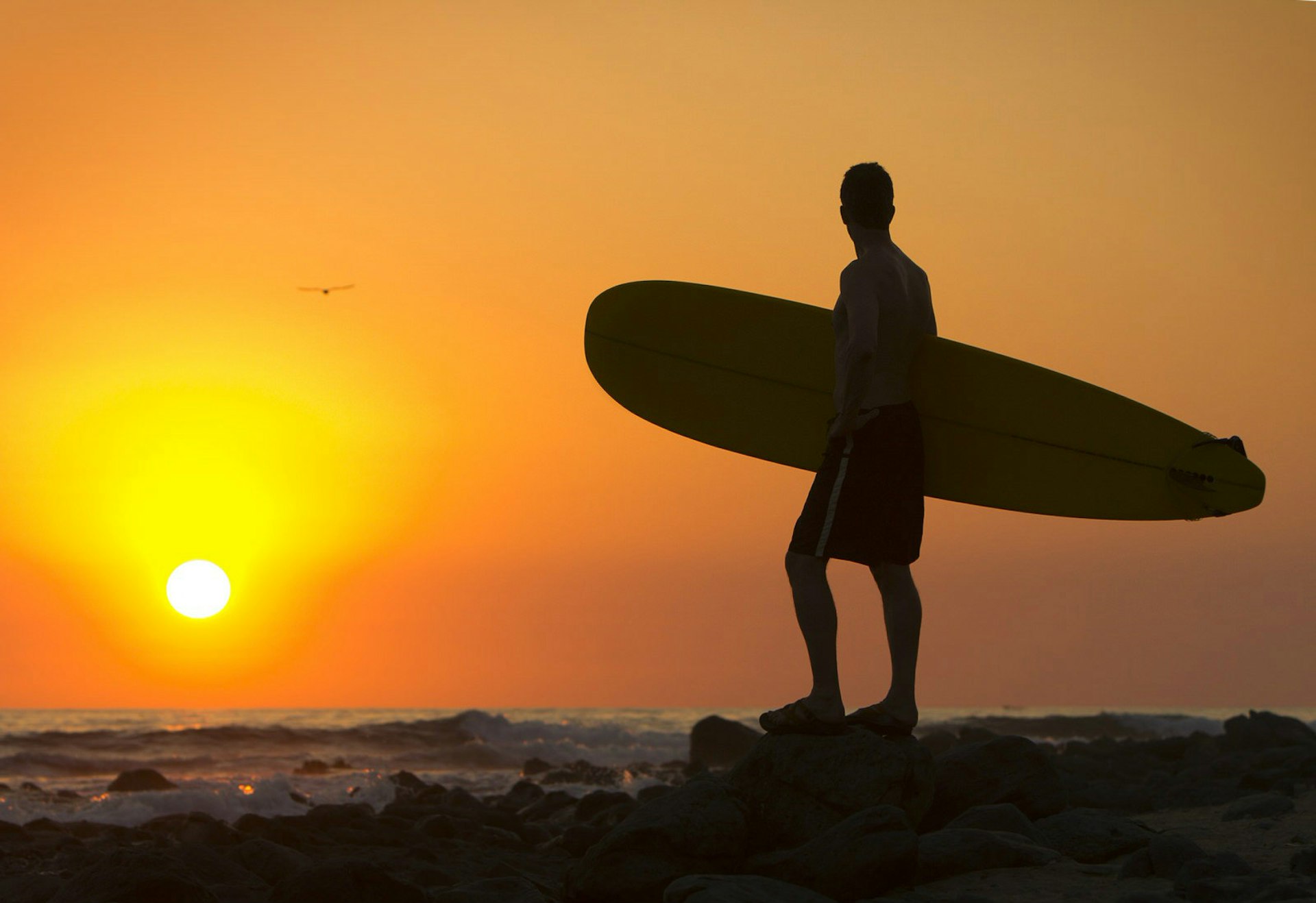 Lesser-known surfing spots – A silhouette of a surfer standing on the shore as the sun sets.