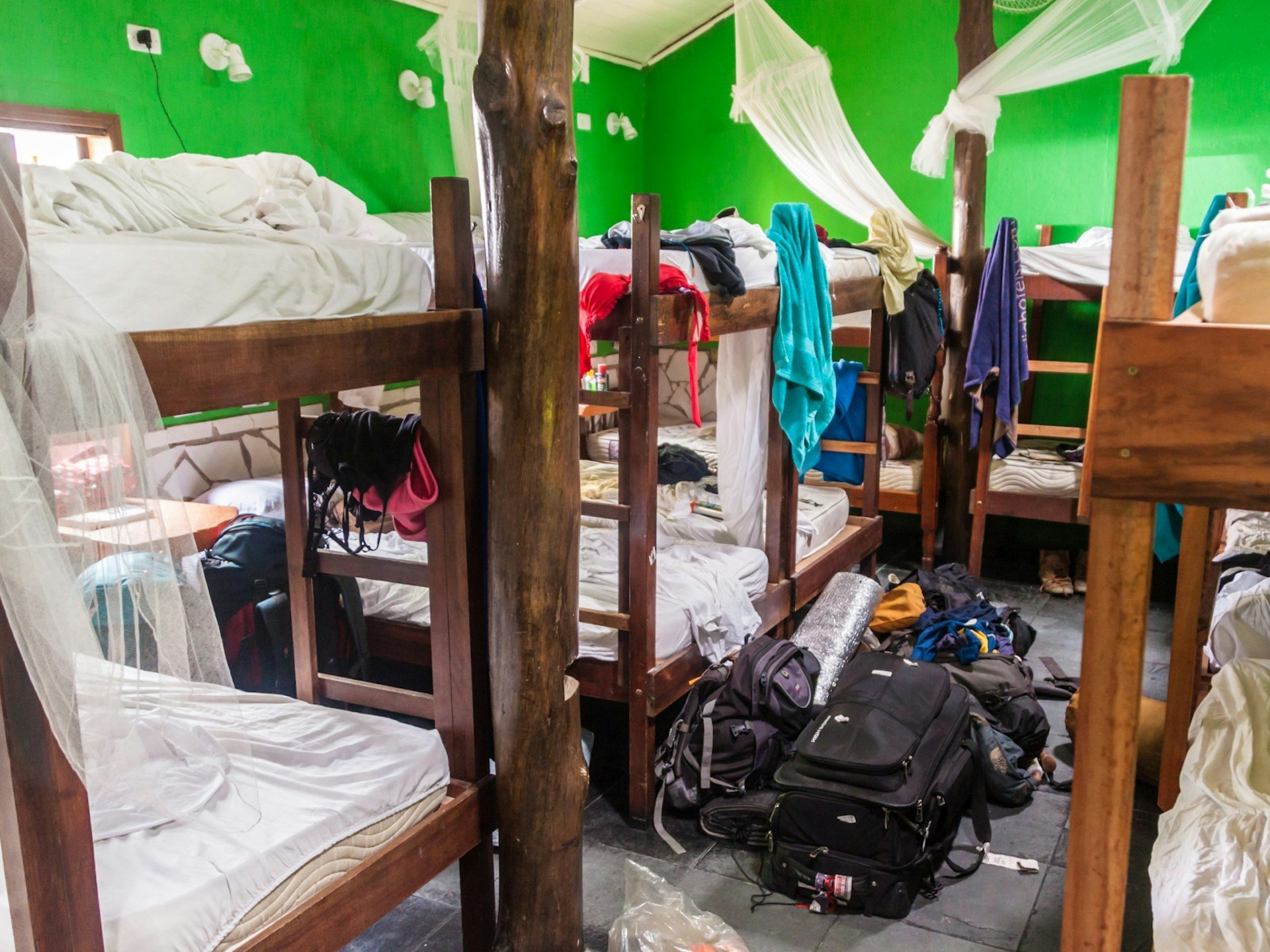 A messy hostel dorm room with suitcases and backpacks on the floor 