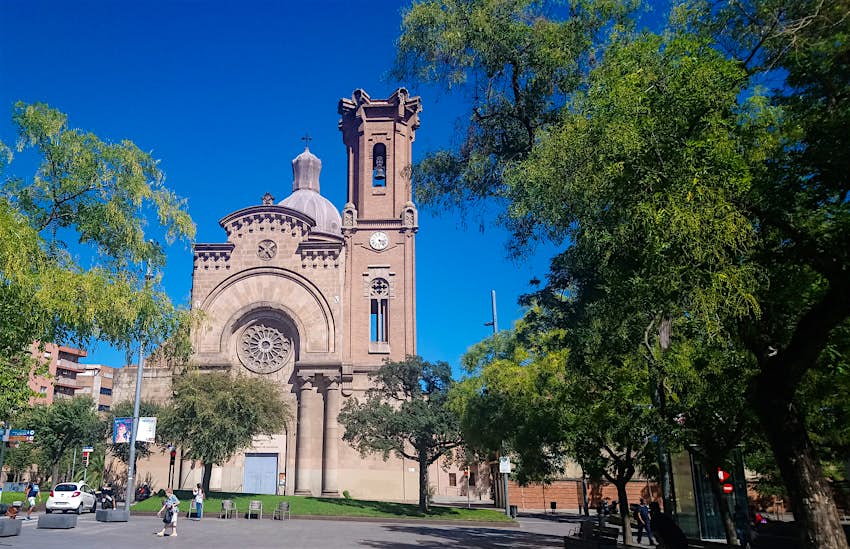 Features - Sant-Andreu-Church-Barcelona-Catalonia-Spain-952699651b07 The pink-hued, neo-Gothic Church of Sant Andreu in Barcelona; the church has a tower and a rose window and sits in a leafy square.