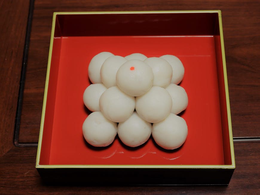 A small pile of white ball-shaped, dough-like treats are placed on a red square plate. Tsukimi Dango is Japanese traditional sweet that's eaten at moon viewing parties.