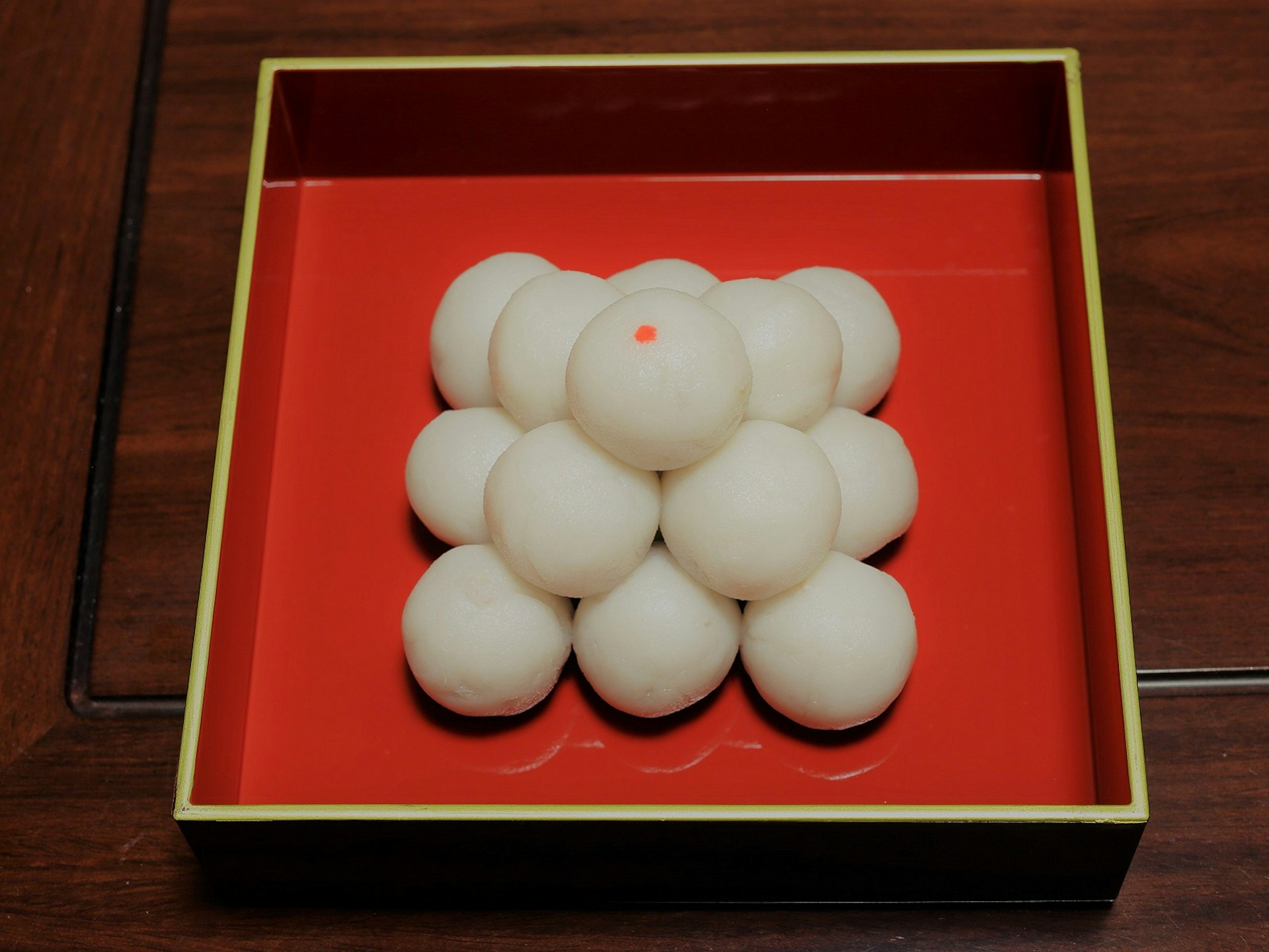 A small pile of white ball-shaped, dough-like treats are placed on a red square plate. Tsukimi Dango is Japanese traditional sweet that's eaten at moon viewing parties.