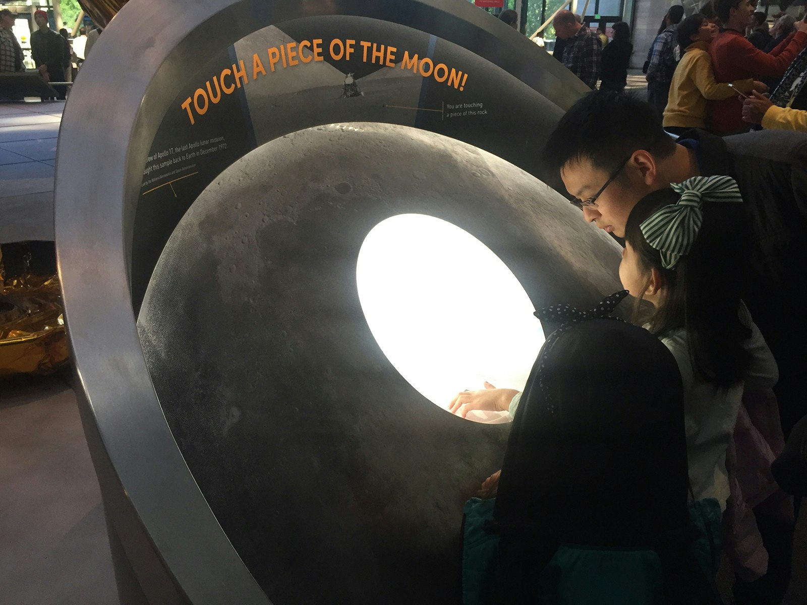 A man and two girls reach out to touch the Moon Rock at the Smithsonian