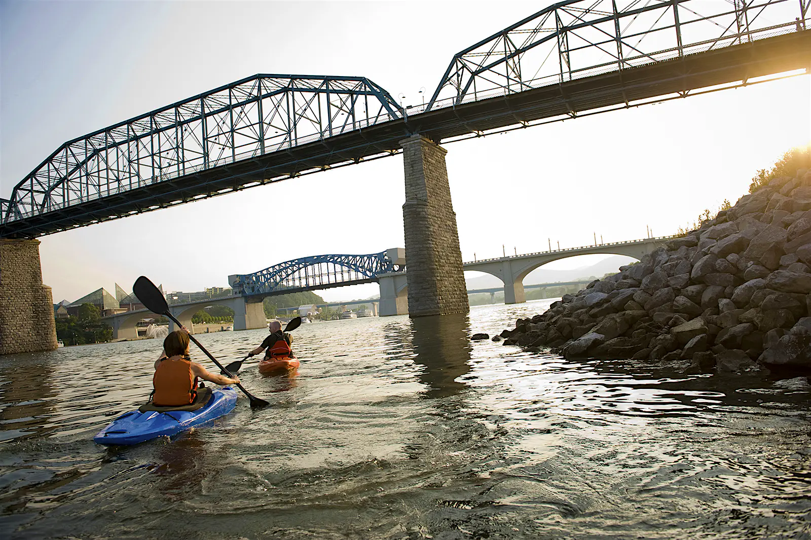 Features - Two kayakers paddle a river near a city. a man and a woman paddle the Tennessee River beneath the Walnut Street Bridge in Chattanooga.