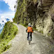 A cyclist rides on Bolivia's Death Road. In the background a condor circles over the scene.