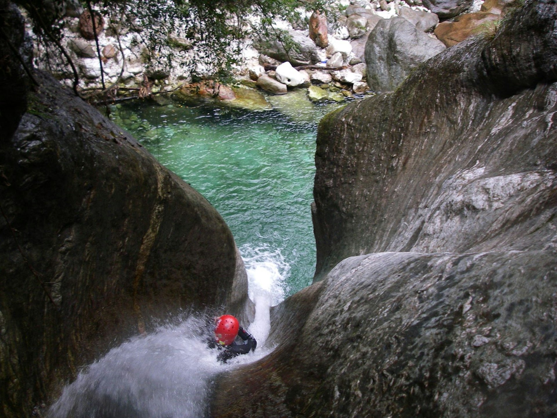 A red-helmeted canyoner slides down a steep water chute © Toscana Adventure Team
