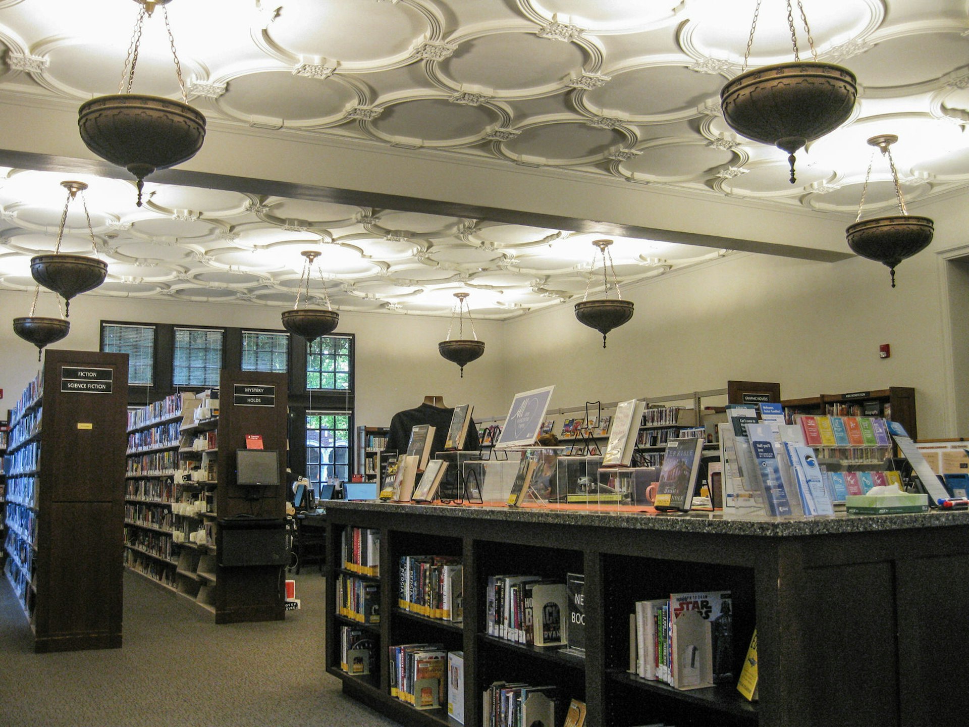 The interior of the Multnomah County Library, with bookshelves and long windows in the background, looking out over a central desk.