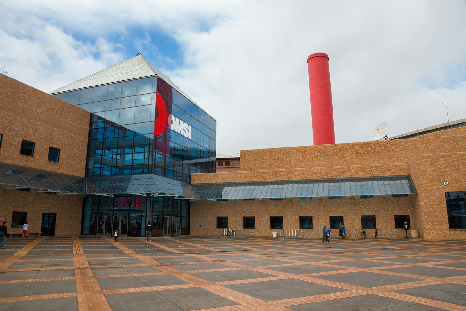 A shot of the facade of the OMSI museum in Portland, with the entrance in a large glass cube and a bright red smokestack.