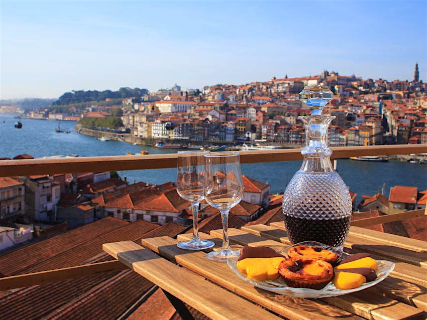 A carafe of port wine and a plate of pastel de nata in a cafe overlooking the city of Porto, Portugal
