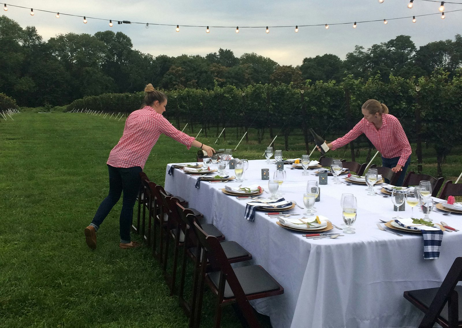two women pour water into glasses on a beautifully set table at twilight in Glen Mills Pennsylvania