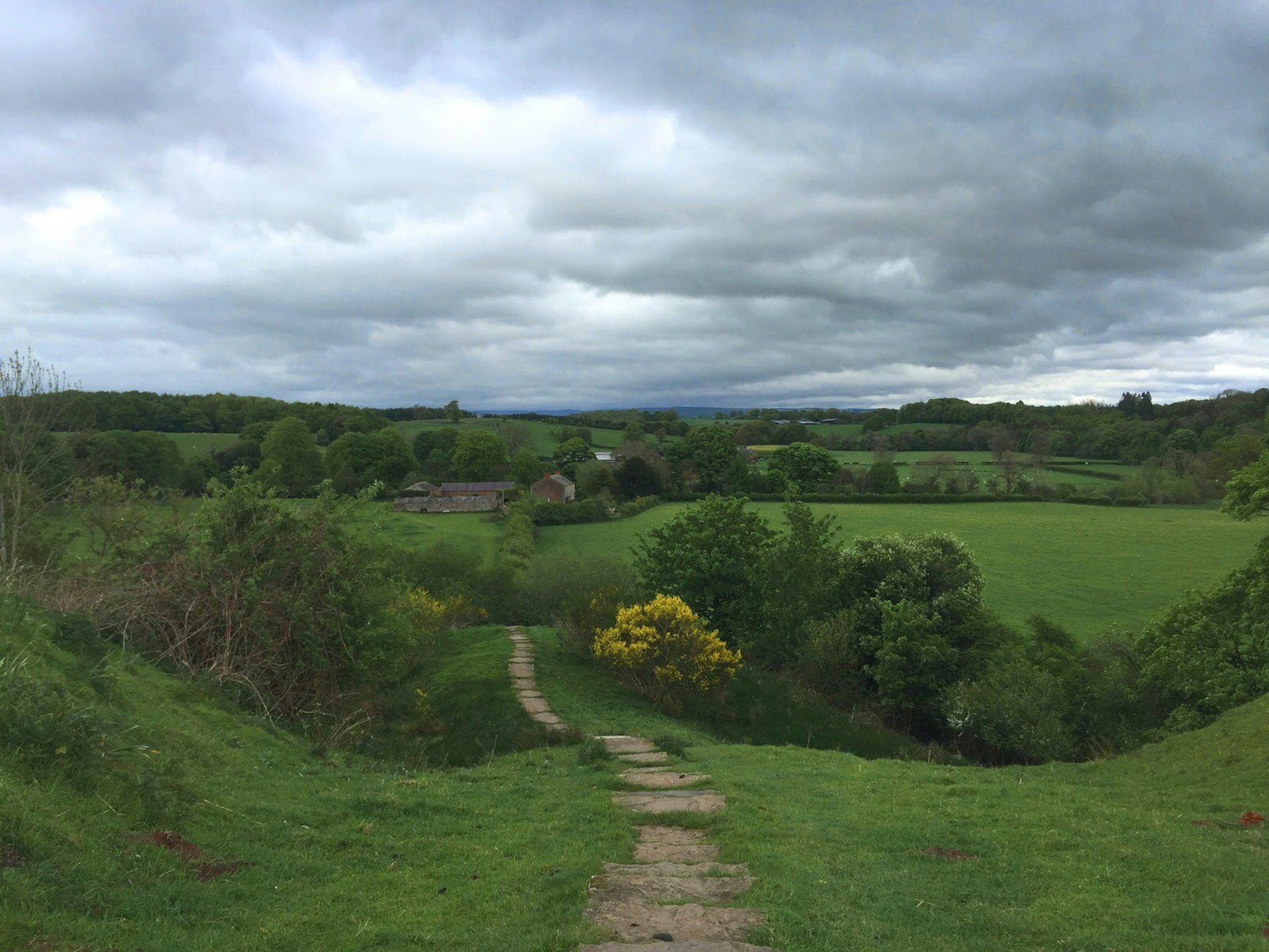 A footpath curves through a valley with grey clouds overhead
