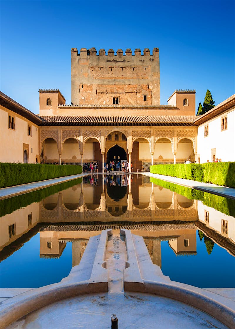 Part of the Alhambra complex - a Moorish-inspired fort with a graceful cloister in the foreground - reflects off the courtyard pool in Generalife Gardens, Granada, Spain.