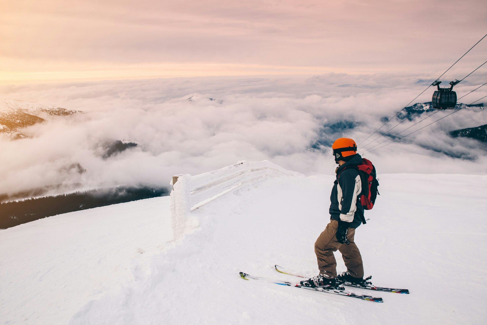 Skier at the summit of a mountain in Slovakia; there is cloud cover below and a chairlift rising to the right.