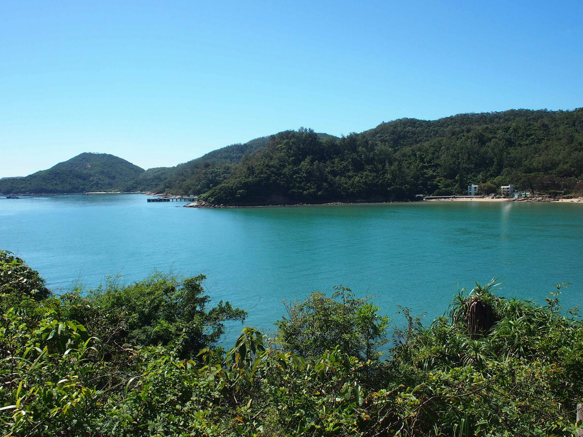 View of turquoise sea, green plants and mountains beyond