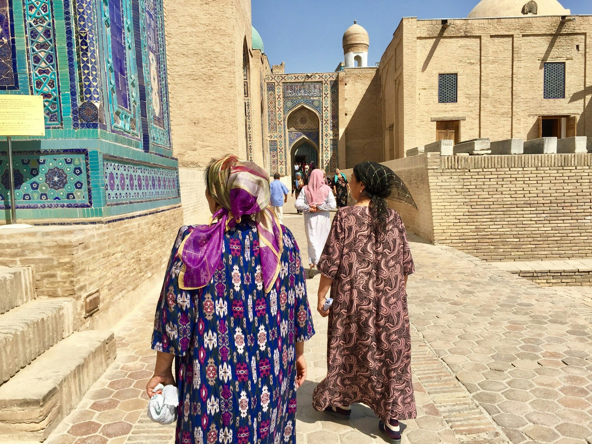 Ladies in bright clothing and head scarves walk through Shah-i-Zinda tiled mausoleum 