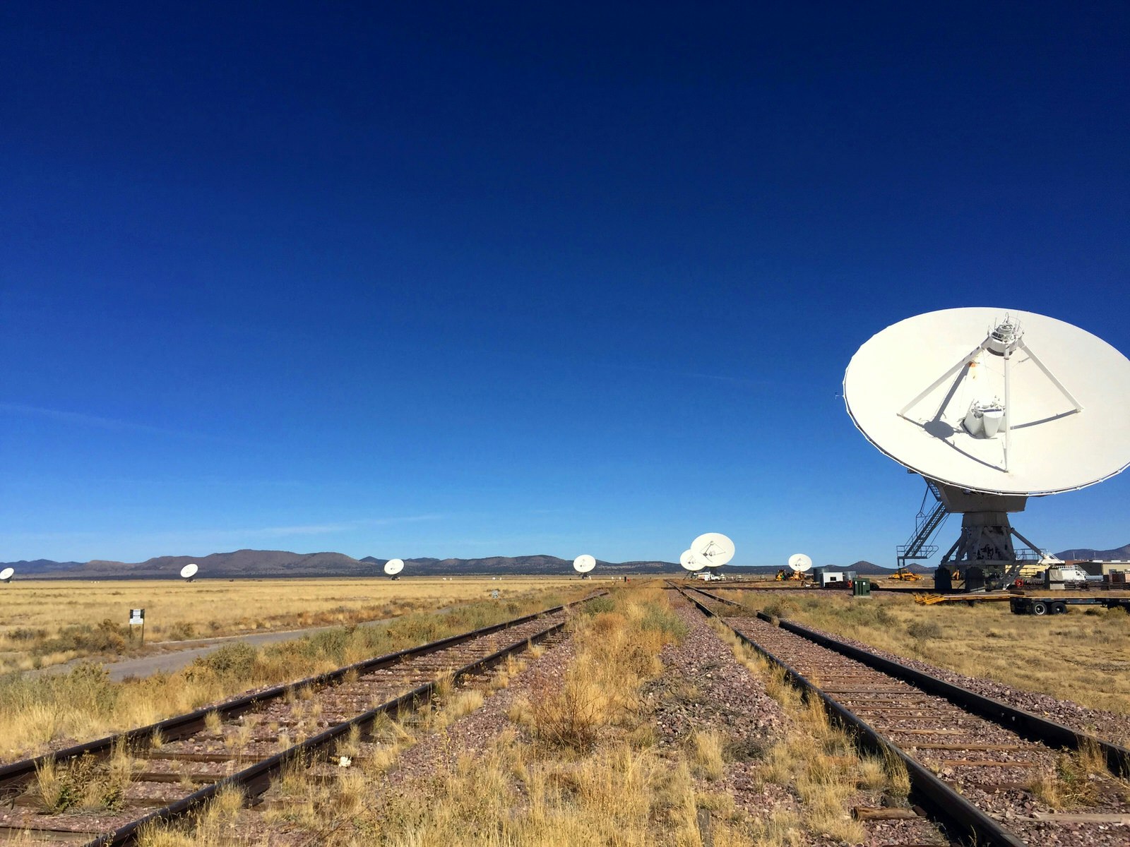 Two sets of railroad tracks next to a series of large white satellite dishes in the desert; Stargazing Southwest USA