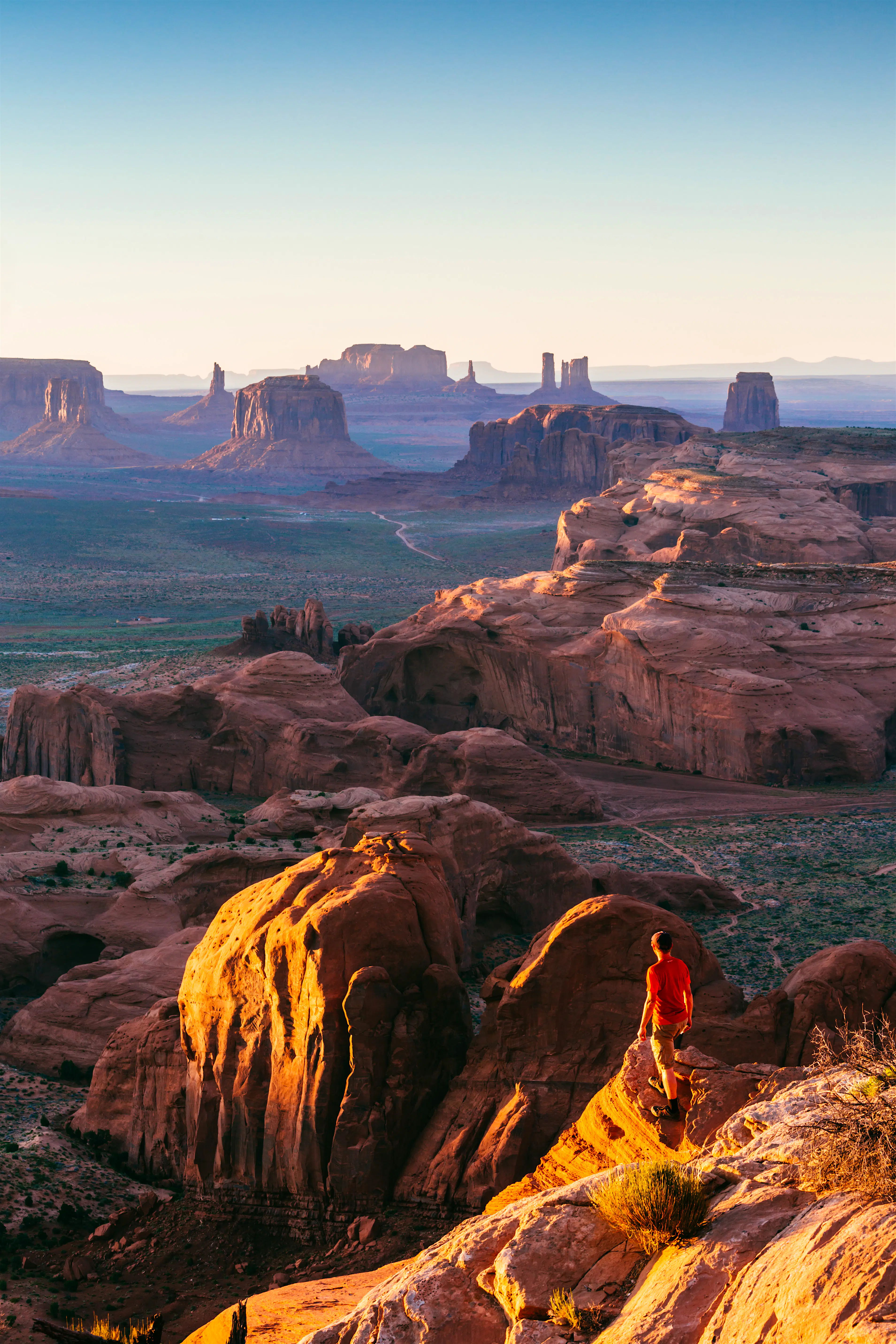 Features - Man looking at the Monument Valley, Arizona, USA A man stands on a cliff overlooking numerous rock formations dotting a desert landscape
