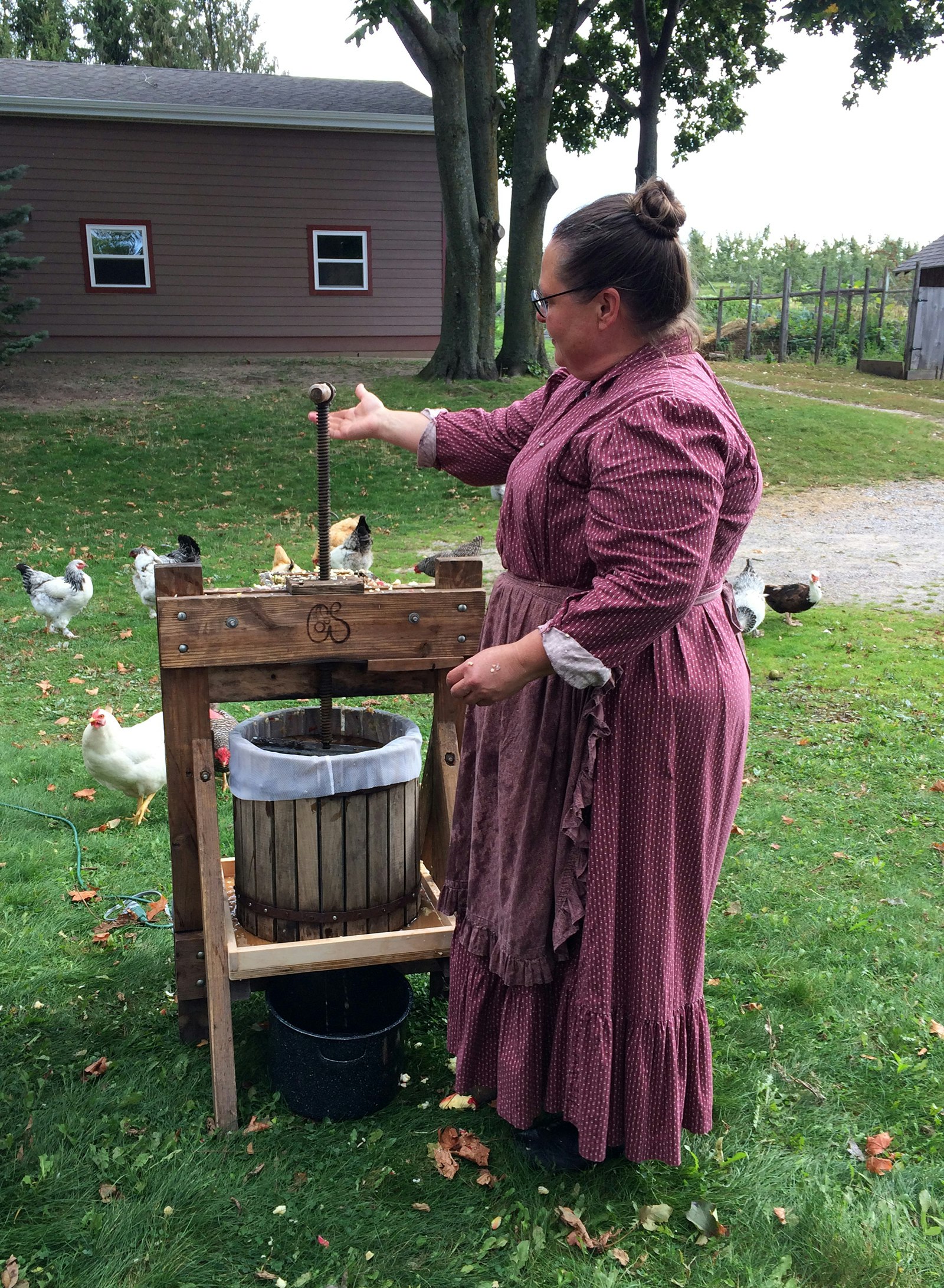 woman in an early 20th-century dress presses cider at a farm homestay in Michigan