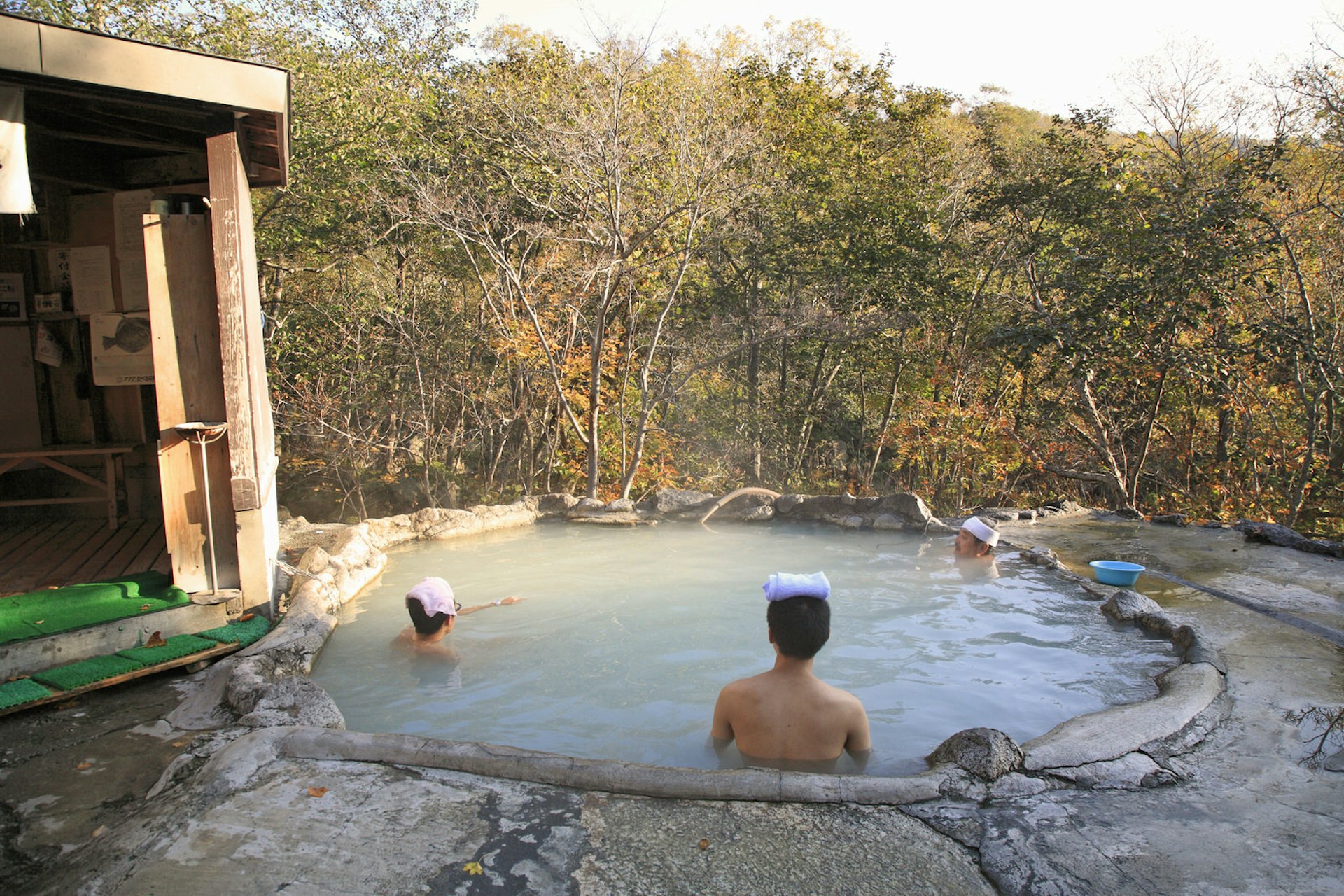 Three people sitting in the Kuma-no-yu hot spring, looking out onto a wooded area