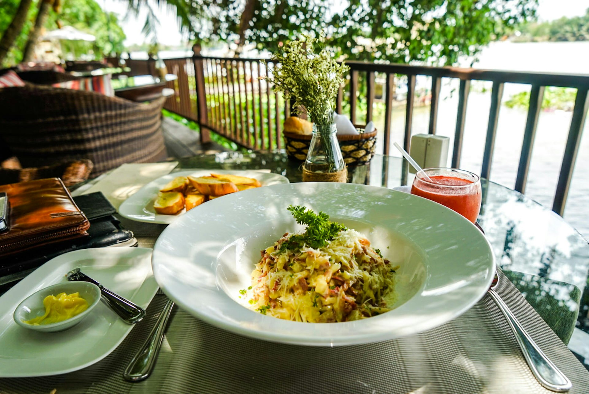 A dish of spaghetti carbonara shown on a table overlooking the river at An Lam Retreats Saigon River