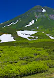 A road leads through a lush green landscape towards mountain Rausu-dake