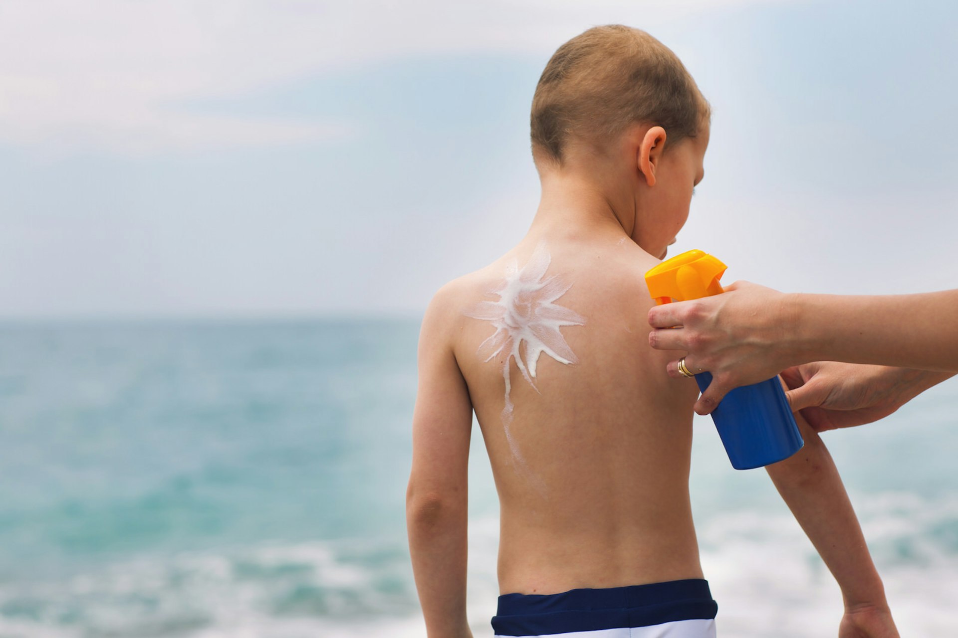 Boy on a beach having sunscreen applied to his back © adriaticfoto / Shutterstock