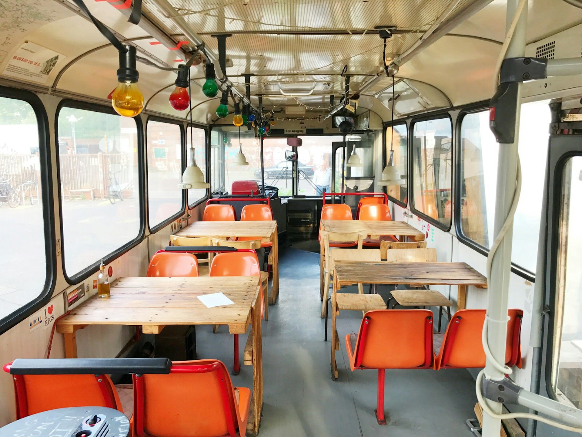 The inside of one of Cafe Pförtner's dining spots on a converted bus. The bus has been refitted with wooden tables, orange school chairs and colourful fairy lights © Jennifer Sojka / Lonely Planet