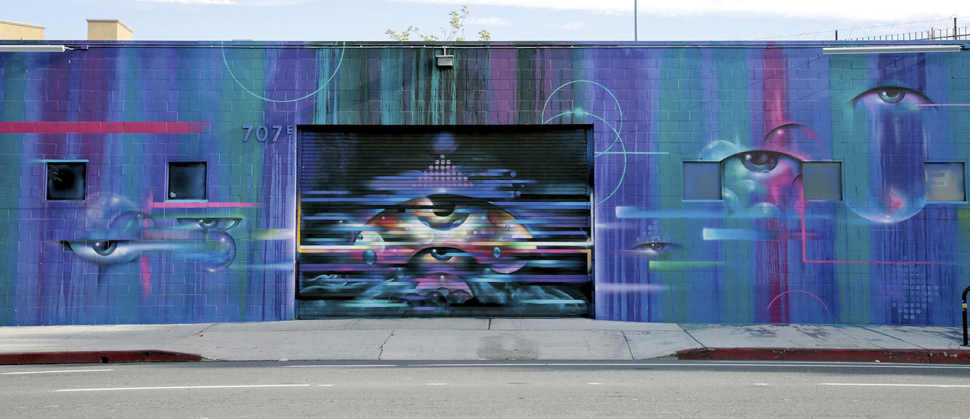 A blue and purple graffiti painting, with what appears to be an eye looking out at the viewer, decorates the outside of warehouse bar EightyTwo.