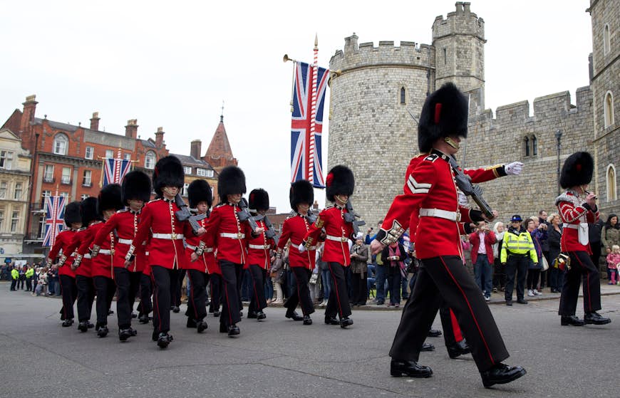 Soldiers in red coats and bearskin hats march in front of Windsor Castle for the Changing of the Guard ceremony in Windsor, England