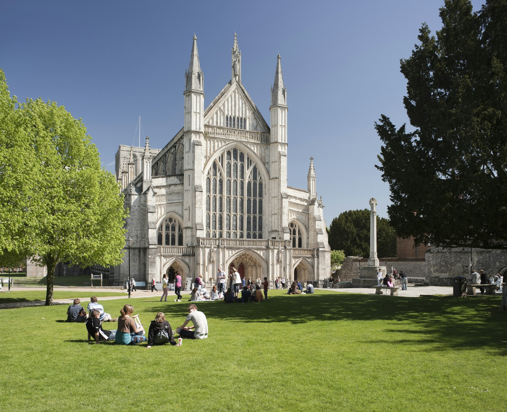 People sit on the grass on a sunny day in front of Winchester Cathedral in Winchester, England