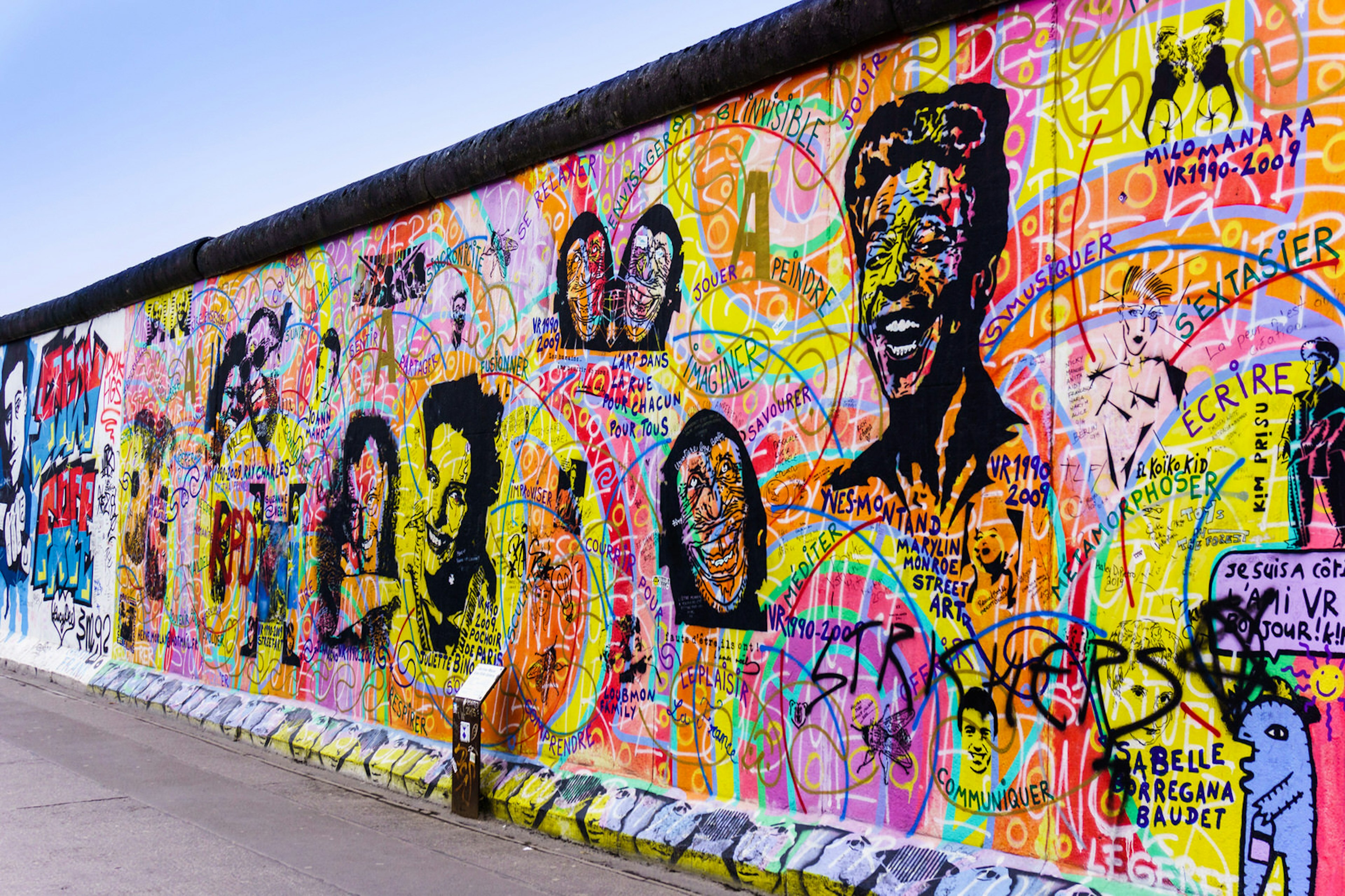 Portraits daubed in black sit on a background of chaotic psychedelic graffiti on a preserved stretch of the east side of the Berlin wall - Lonely Planet © Ewais / Shutterstock