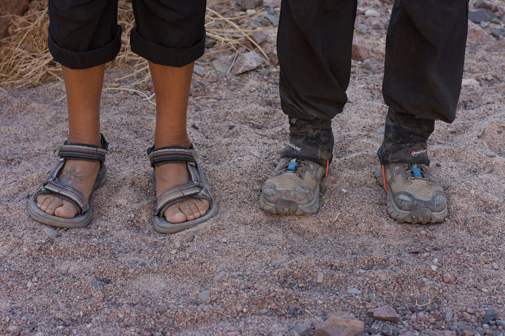 A Bedouin guide - clad in a pair of well-worn sandals - stands next to a hiker in padded hiking boots © Jen Rose Smith / Lonely Planet