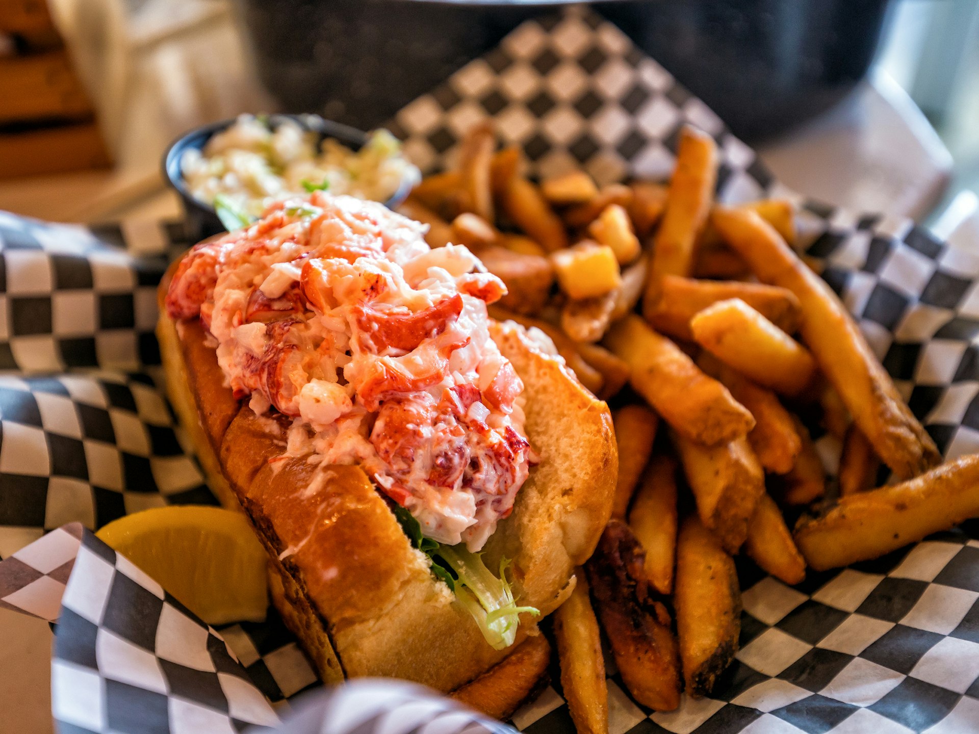 A Maine lobster roll in a basket with a side of fries