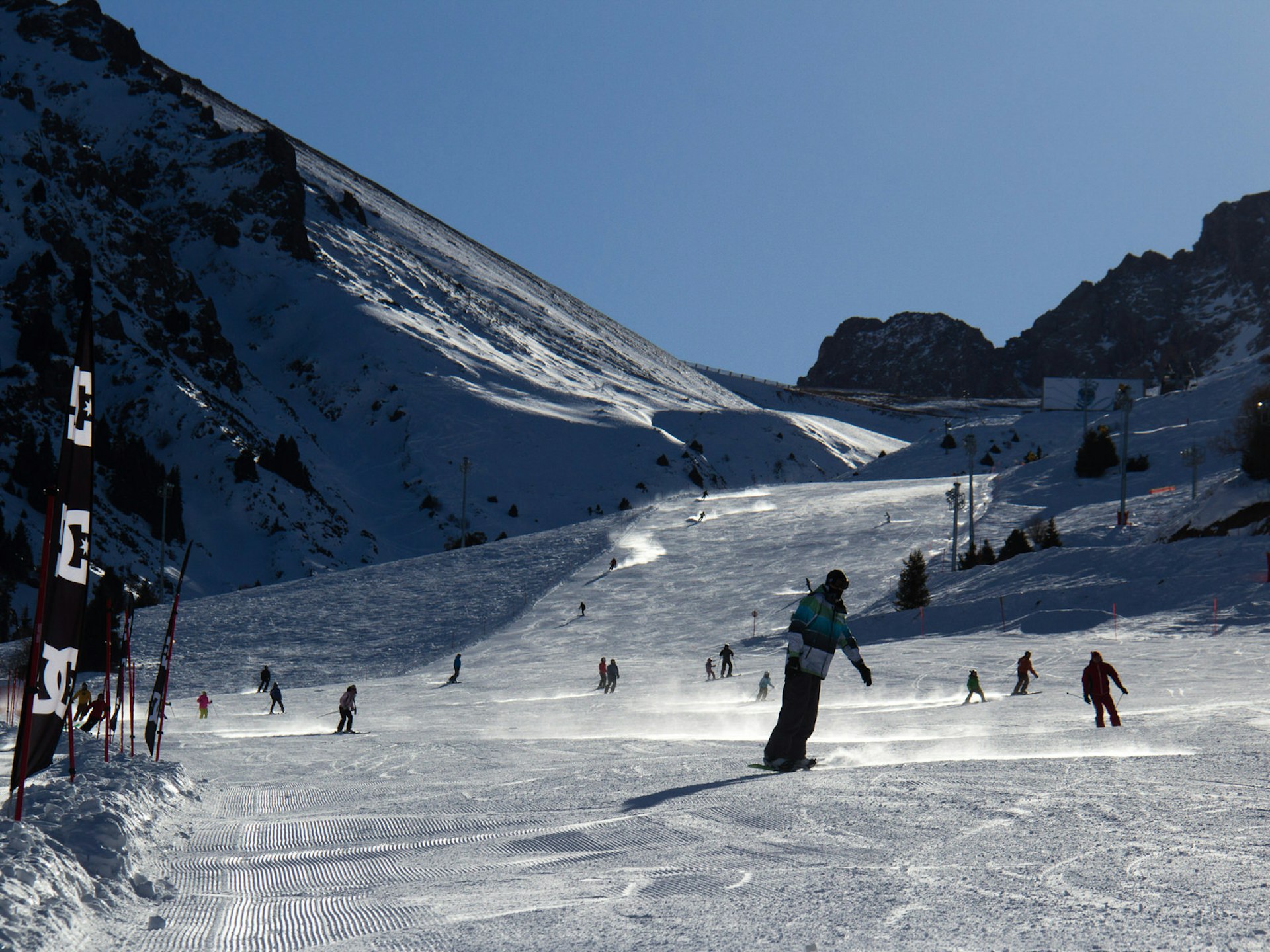 Skiers and snowboarders coasting down a snowy piste with blue sky in the background at Chimbulak Ski Resort near Almaty © Stephen Lioy / ϲʼʱ