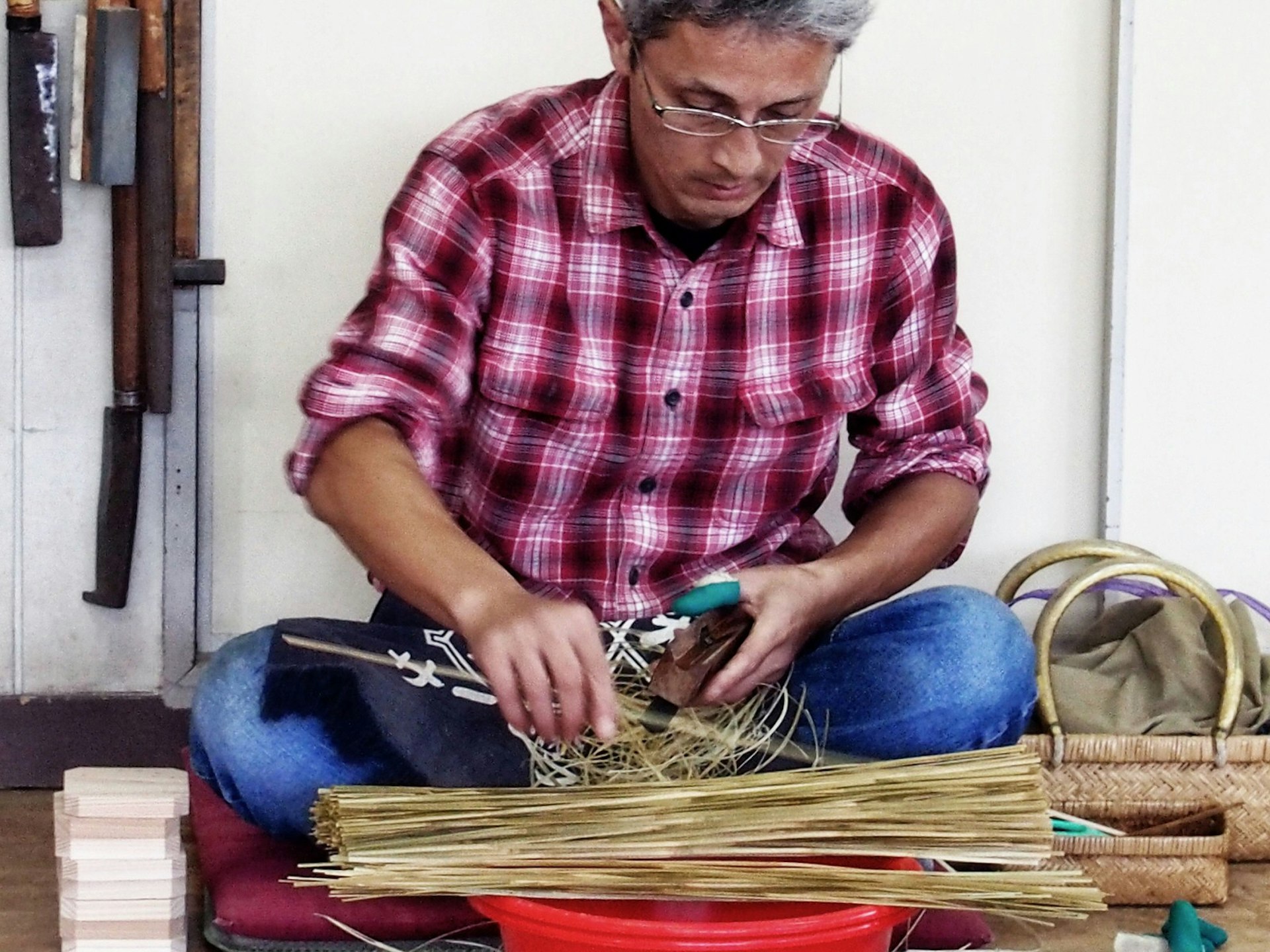 A craftsman sits sorts and cuts through a pile of bamboo strips © Manami Okazaki / Lonely Planet