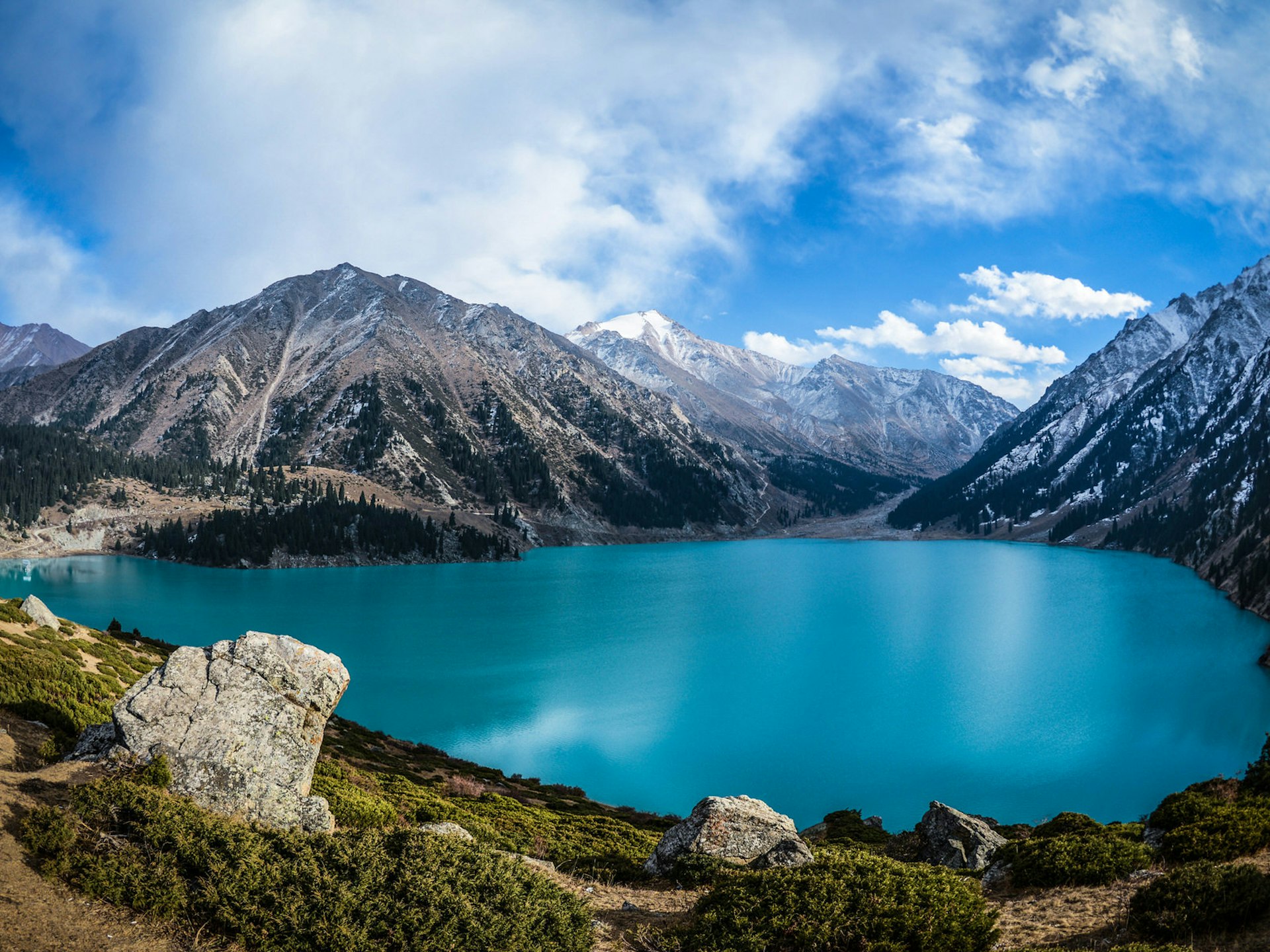 A turquoise lake surrounded by snow-capped mountains and blue sky © Aureliy / Shutterstock