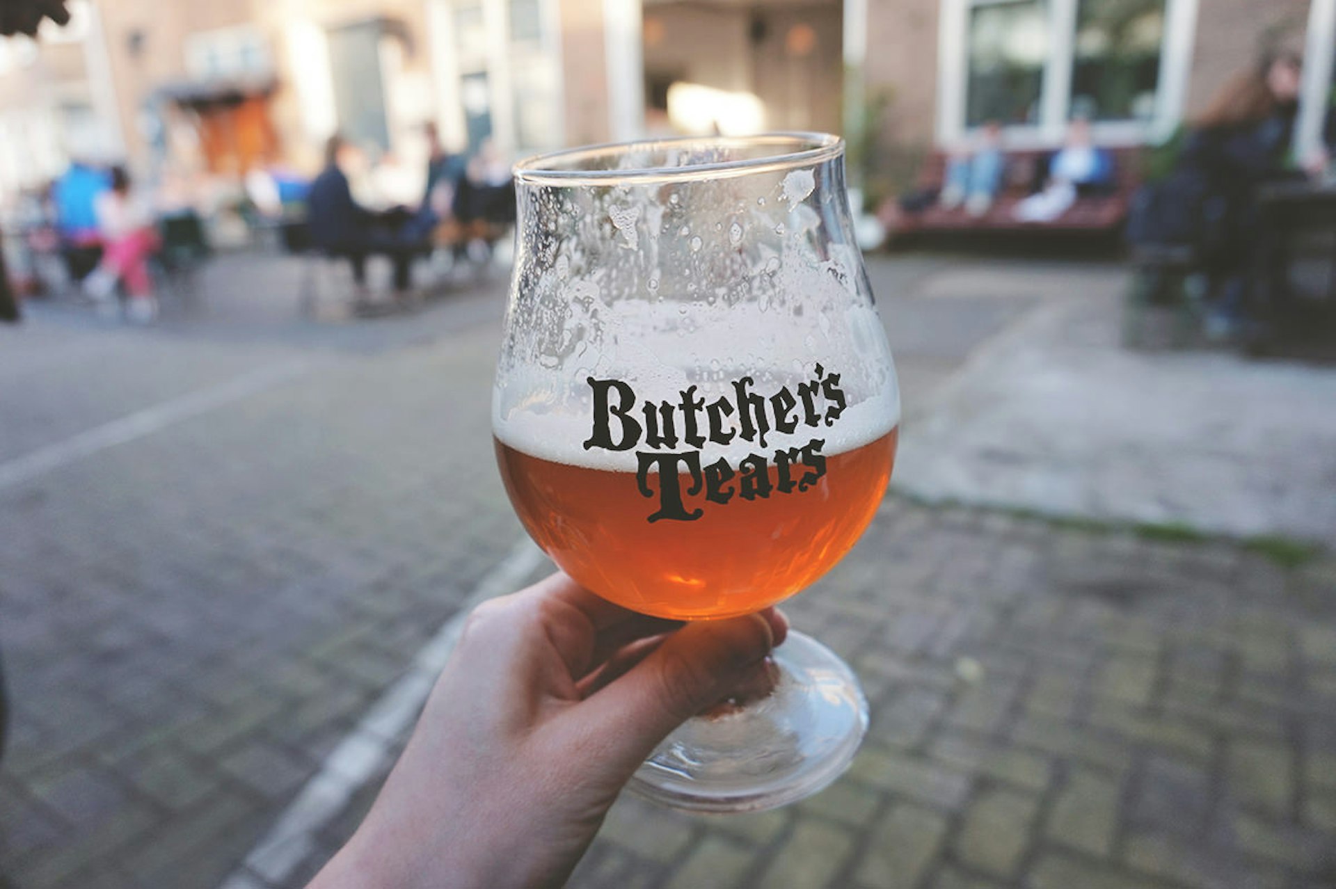 A half-full glass of beer with the Butcher's Tears bar logo on it in Amsterdam, the Netherlands