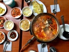 A table with several dishes of food including a large pot of spicy red kimchi stew at Gwanghwamun in Seoul.