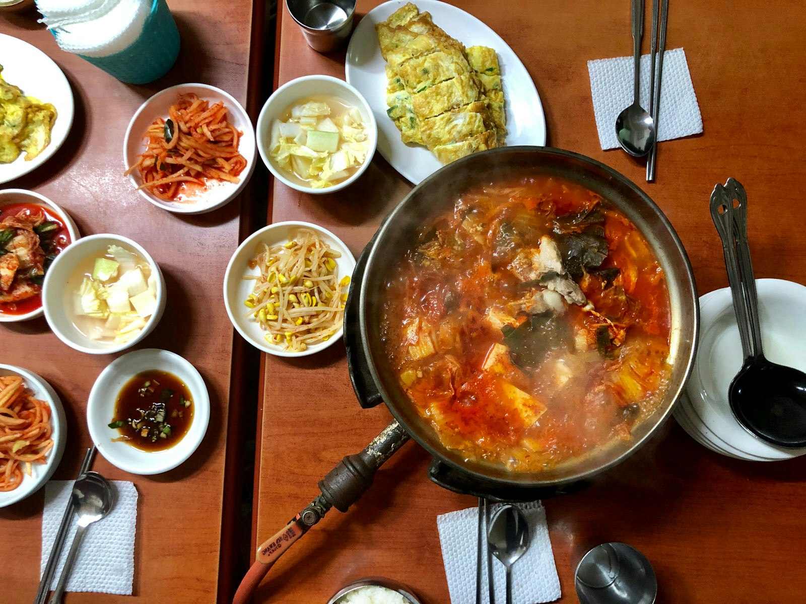 A table with several dishes of food including a large pot of spicy red kimchi stew at Gwanghwamun in Seoul © Hahna Yoon / Lonely Planet
