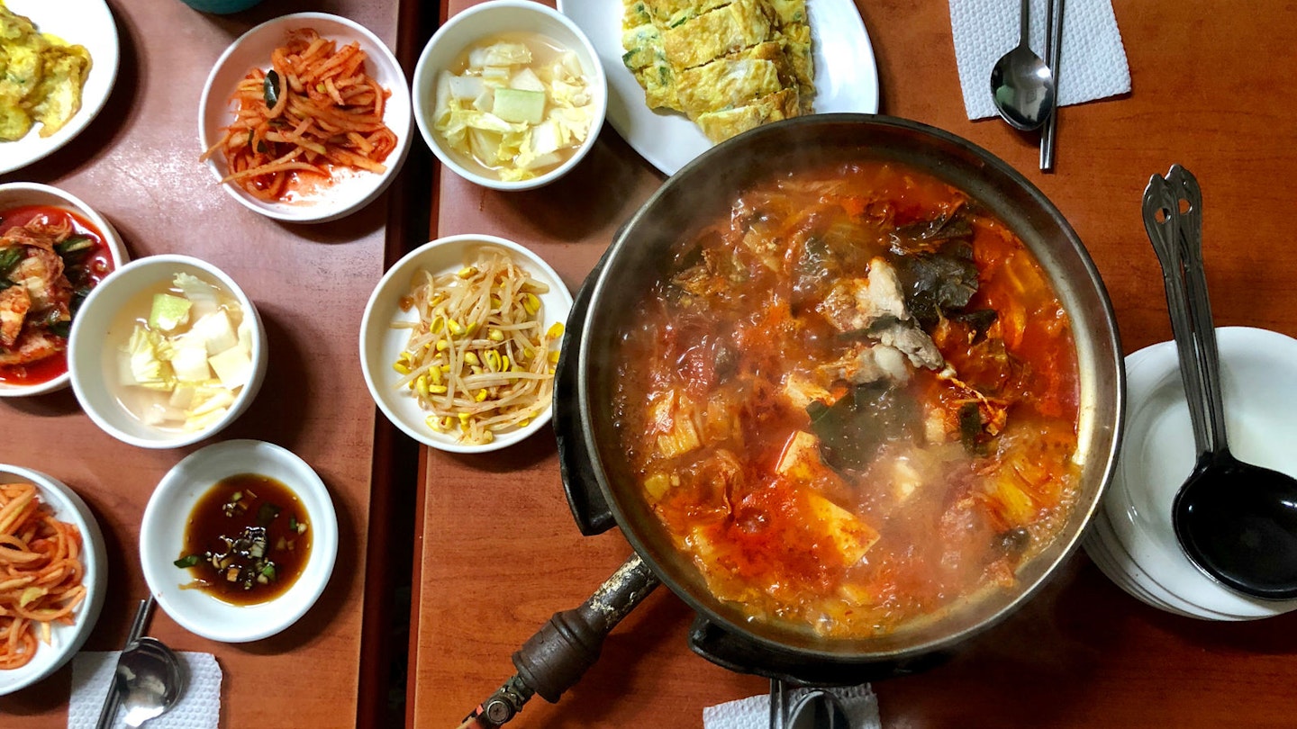 A table with several dishes of food including a large pot of spicy red kimchi stew at Gwanghwamun in Seoul.