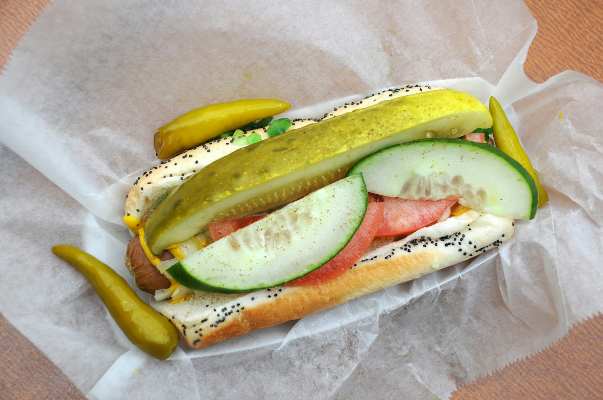 top-shot of a hot dog served Chicago-style with peppers and cucumbers in a poppy seed bun
