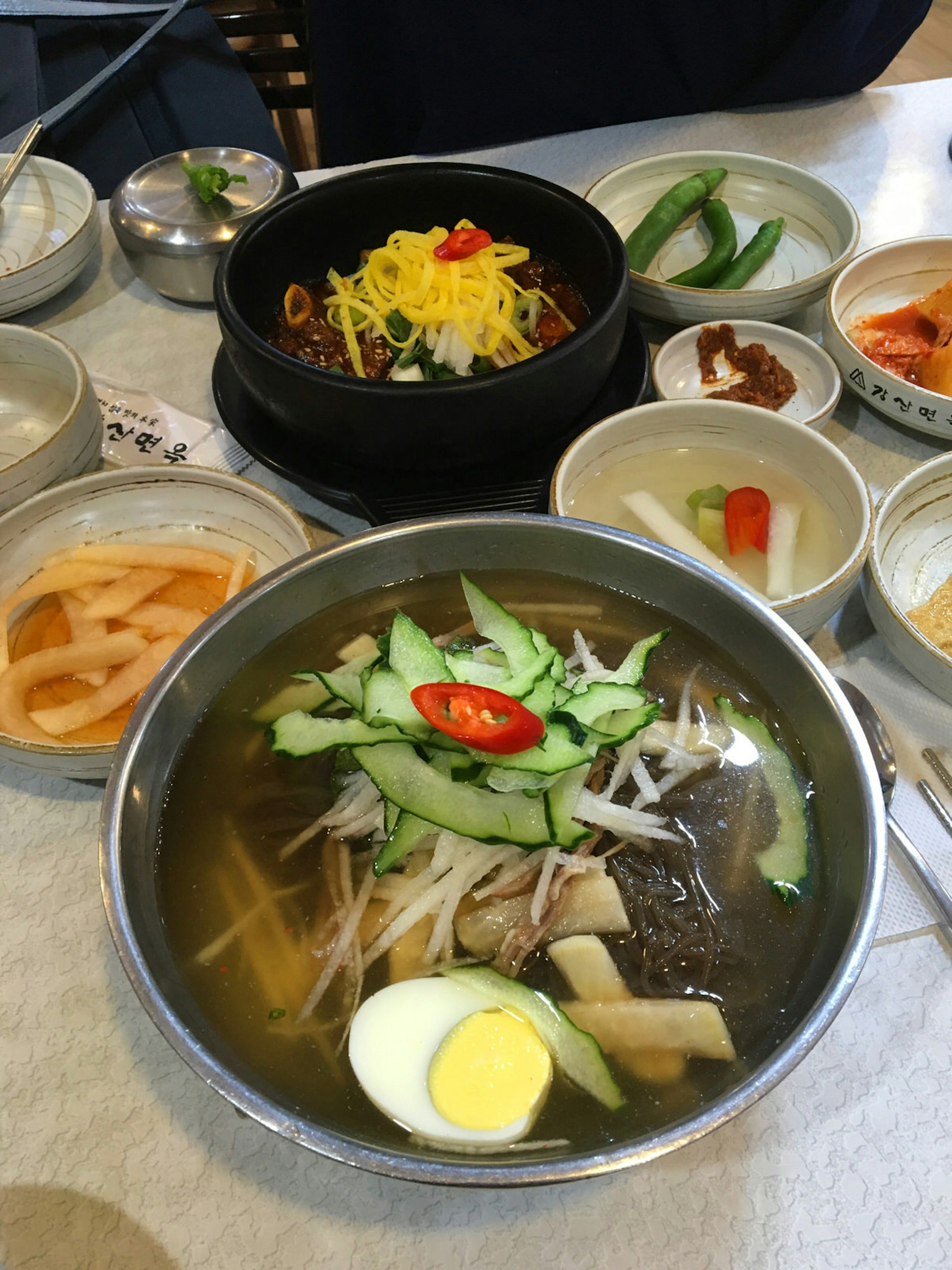 A bowl of North Korean-style iced noodles with an egg in broth on a table with several other small Korean dishes at Kangsan © Hahna Yoon / Lonely Planet