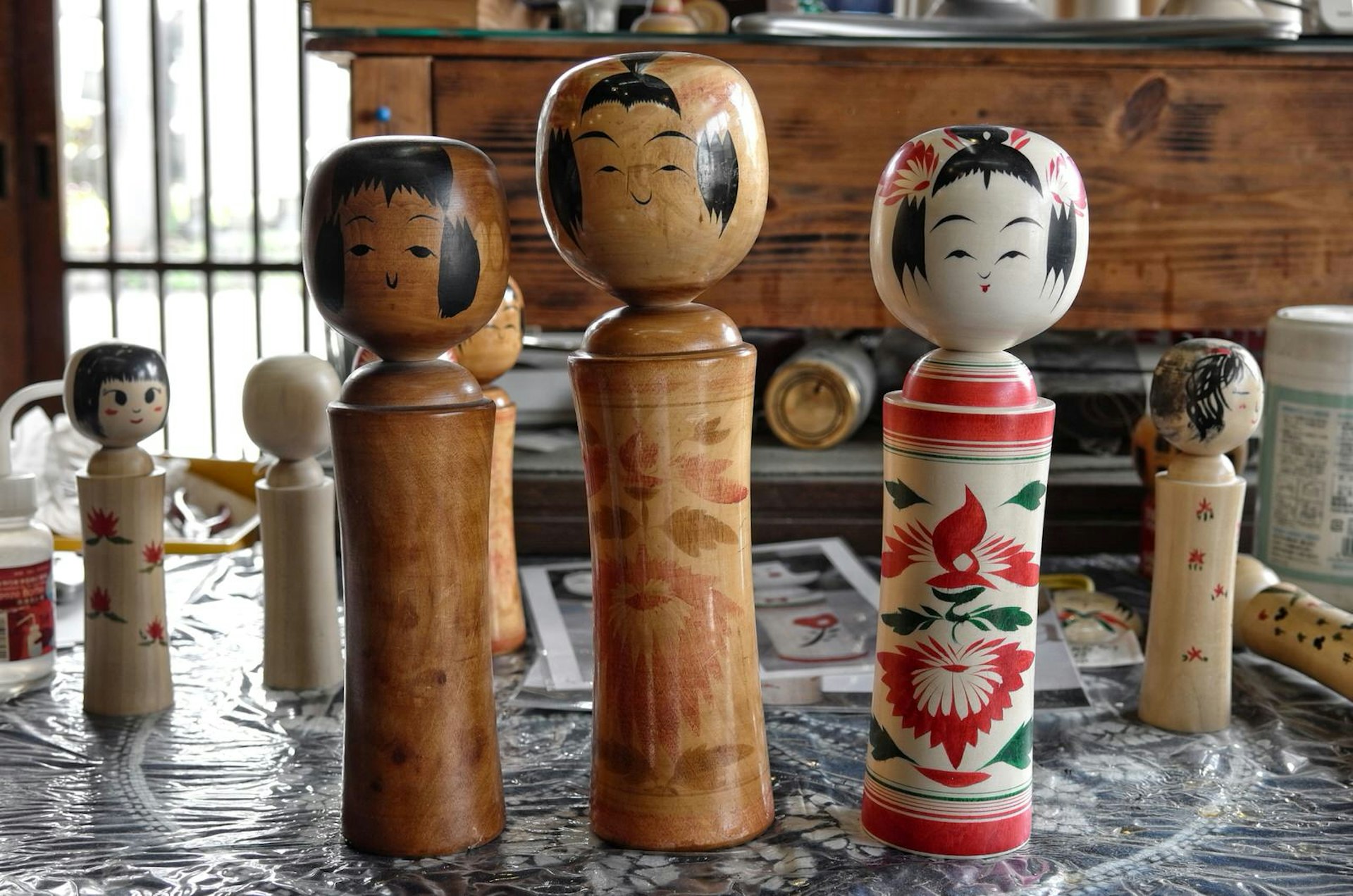 Three kokeshi dolls, made by three generations of artisan, stand on a table in the workshop of Yasuo Okazaki © Manami Okazaki / Lonely Planet