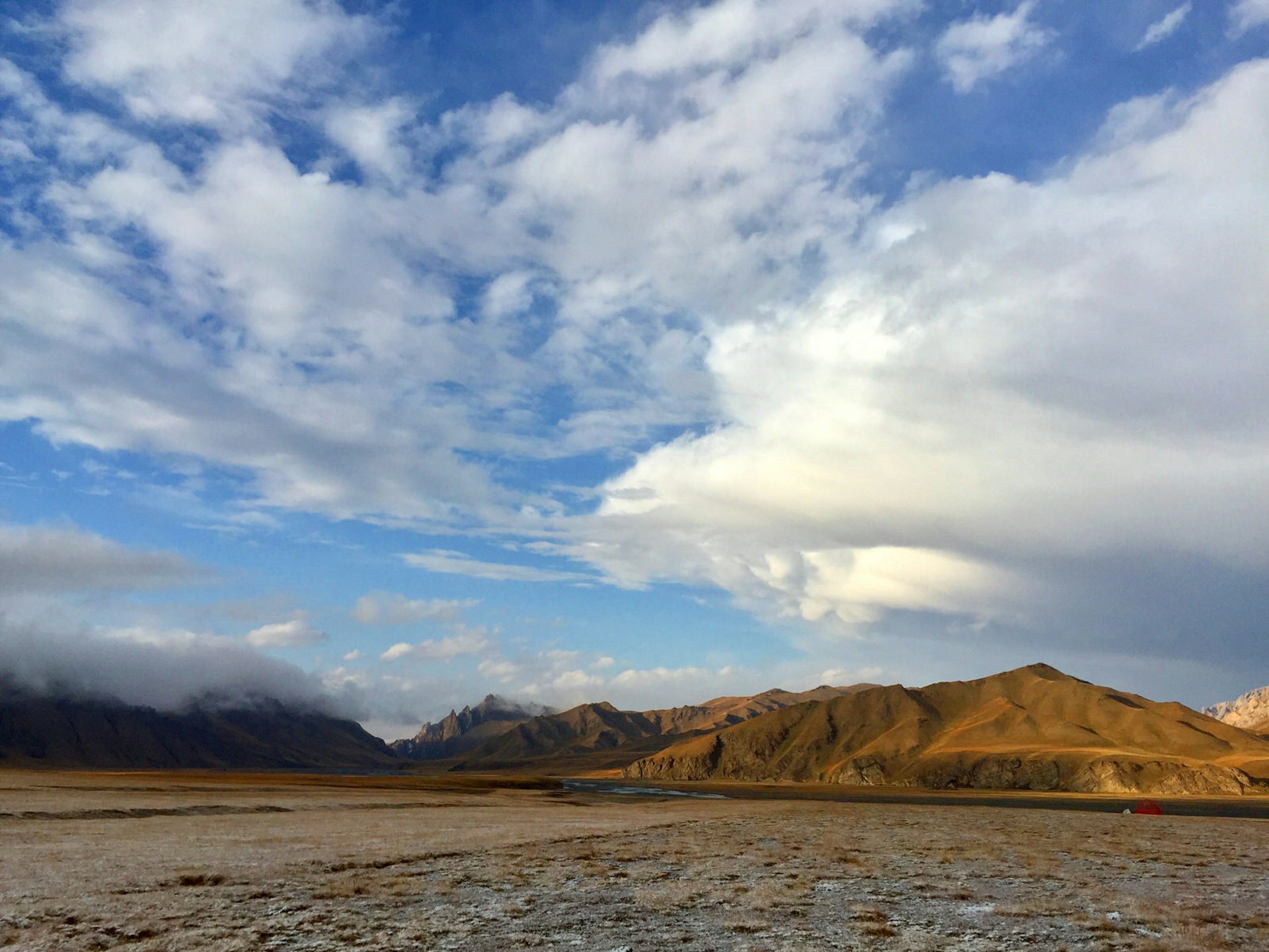 Wide landscape shot of brown mountains, a valley dusted with snow and blue sky dotted with white clouds © Megan Eaves / ϲʼʱ