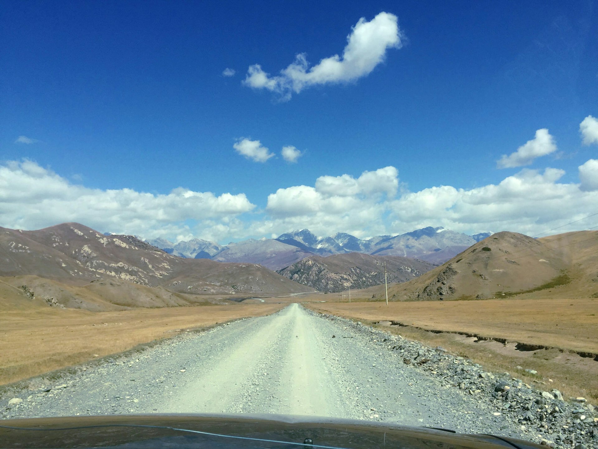View through the windscreen of an SUV onto a wide dirt road leading into mountains, with blue sky above © Megan Eaves / Lonely Planet