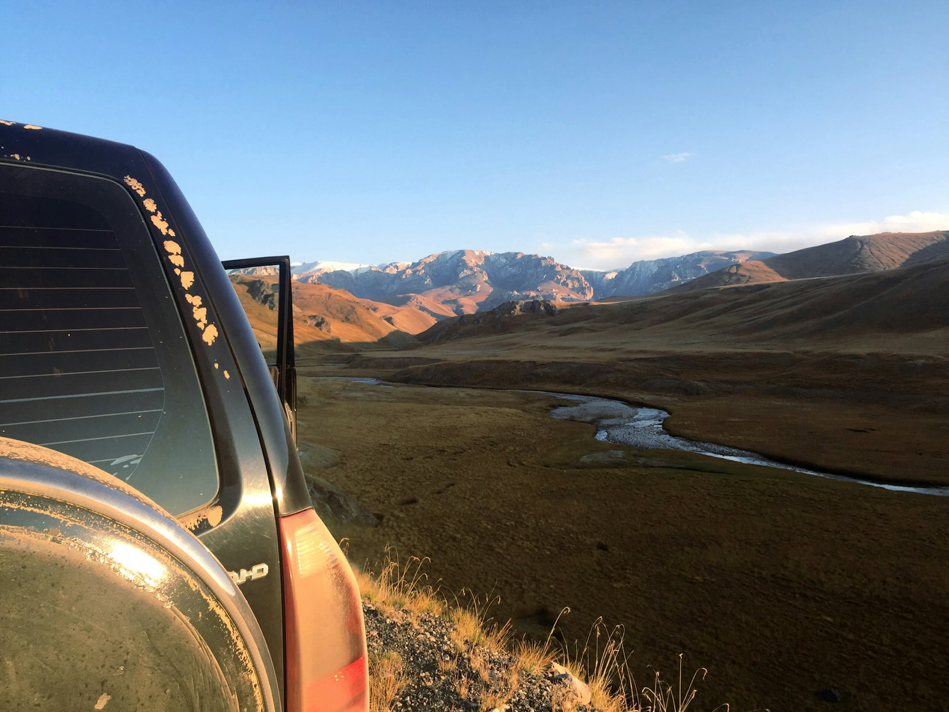The back of a black SUV with its door open and further a view over a valley with a river and mountains in the distance © Megan Eaves / Lonely Planet