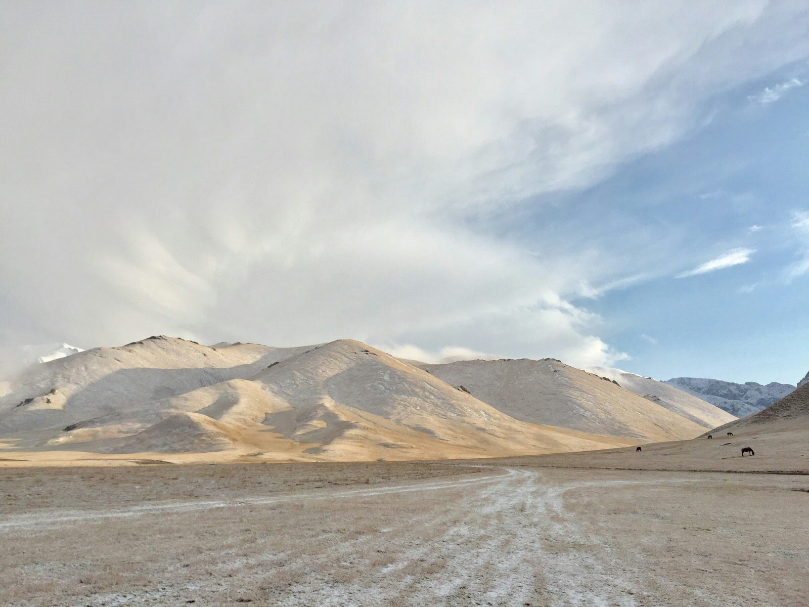 Tan and brown mountains in the distance with a light dusting of white snow, and white clouds above © Megan Eaves / Lonely Planet 