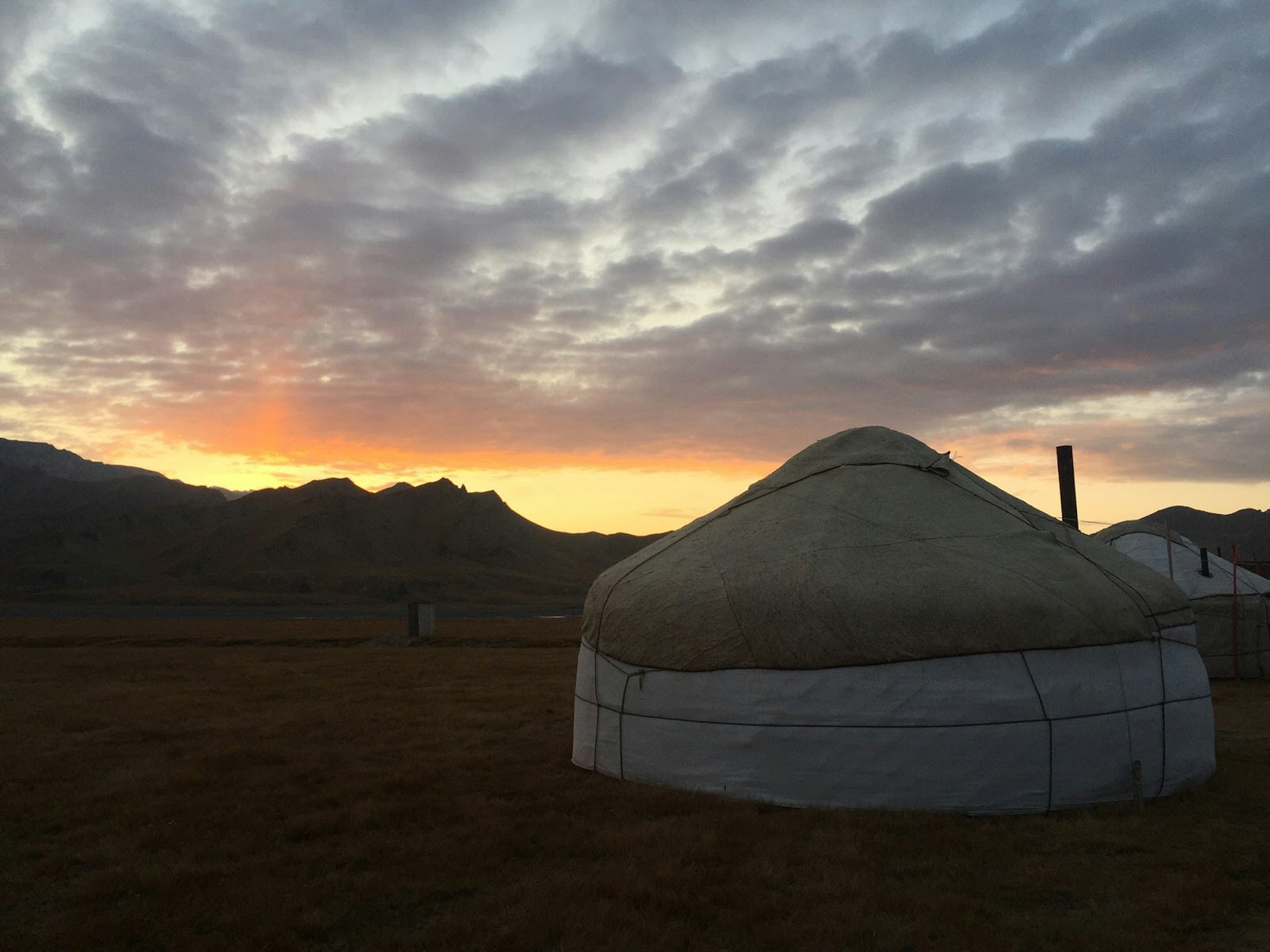 A pink and yellow sunset outlines mountains behind a white yurt tent with small chimney © Megan Eaves / Lonely Planet